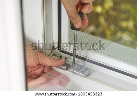 handyman adjusting white pvc plastic window indoors. worker using screwdriver to repair upvc window. homework maintenance. Royalty-Free Stock Photo #1803458323