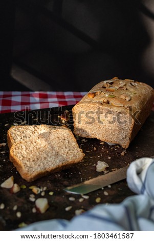Whole grain bread loaf, organic, with nuts and seeds. Slices ready to serve, breakfast table in morning light. Healthy living and home bread making concept. Space for text, vertical