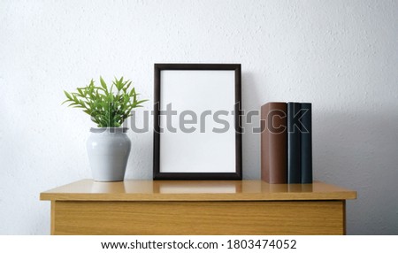 Black frame with plant and books over wooden furniture Royalty-Free Stock Photo #1803474052