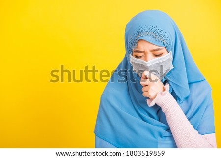 Asian Muslim Arab, Portrait of happy beautiful young woman religious wear veil hijab she wearing protective face mask, outbreak coronavirus use hand close mouth and sneeze, isolated yellow background