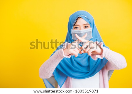 Asian Muslim Arab, Portrait of happy beautiful young woman Islam religious wear veil hijab and face mask protect quarantines disease coronavirus show fingers crossed to x shape no sign isolated yellow