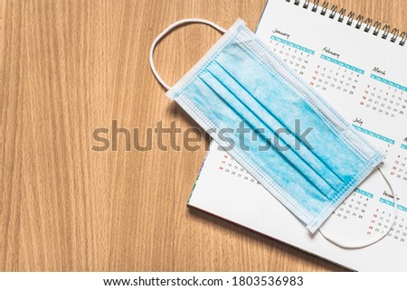 blue surgical face mask with white yearly calendar on wooden desk, top view