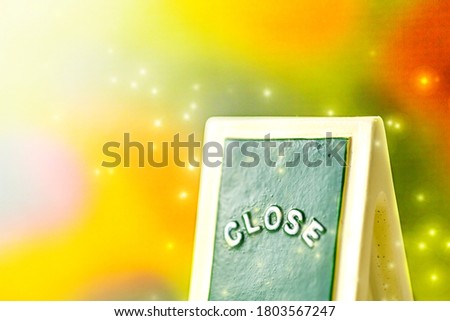 Close up of a green ,yellow with white "CLOSE" chalkboard sign leaning against bright, colorful with sparkle background.