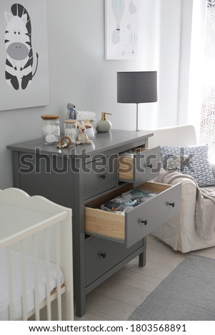 Modern open chest of drawers with baby clothes and accessories in room