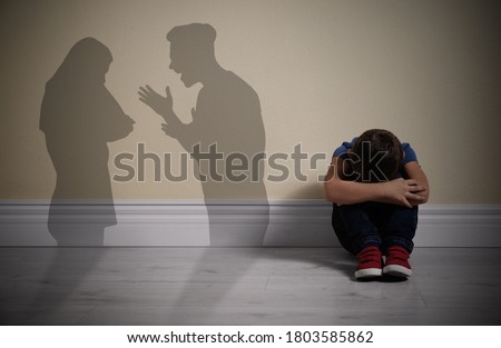 Little boy sitting on floor near yellow wall and silhouettes of arguing parents  Royalty-Free Stock Photo #1803585862
