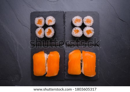 A group of colorful salmon nigiri and salmon roll sushi on dark slate.