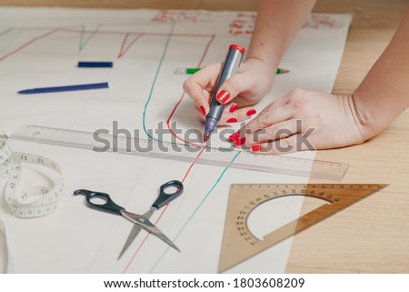 Designer creates a model. Female hands with a manicure do the layout of the sewing pattern on paper
