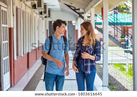Two caucasian teenagers friends happy returning to school speaking along the hallway. Back to school concept.