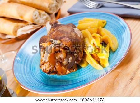 Image of baked pork knuckle with potatoes served on blue plate