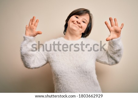 Young down syndrome woman standing over isolated background showing and pointing up with fingers number ten while smiling confident and happy.
