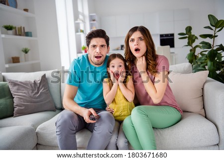 Photo of shocked terrified three people mommy daddy small child girl sit cozy couch remote control switch channel search cartoons find horror scream in house indoors