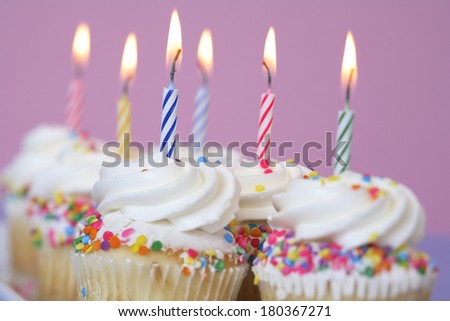 Birthday cupcakes with colored lit candles on purple background