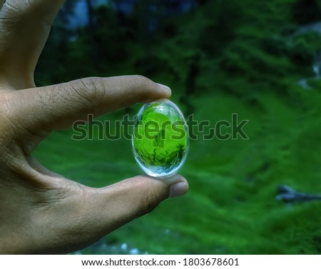 uttarakhand,india-3 june 2020:oval shaped glass.this is a picture of an oval shaped glowing object in hand.this glass looks like a water drop.bright glass in forest.glowing glass in hand.wallpaper. 
