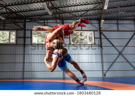 Two greco-roman  wrestlers in red and blue uniform wrestling  on a blue wrestling carpet in the gym Royalty-Free Stock Photo #1803680128