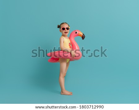 Happy child wearing swimsuit. Girl with swimming ring flamingo. Kid on a colored turquoise background.