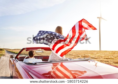 Woman holding an American flag on a road trip                                 Royalty-Free Stock Photo #1803714226