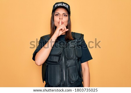 Young beautiful brunette policewoman wearing police uniform bulletproof and cap asking to be quiet with finger on lips. Silence and secret concept.