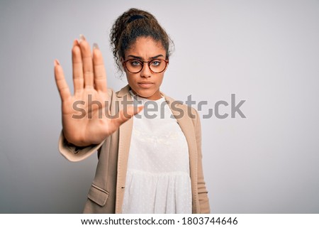 Beautiful african american businesswoman wearing jacket and glasses over white background doing stop sing with palm of the hand. Warning expression with negative and serious gesture on the face.