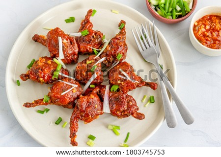 Popular Indo-Chinese Chicken Appetizer Made of Chicken Winglets on a White Plate on White Background Garnished with Scallion and Red Chili Pepper Horizontal Top View Photo Royalty-Free Stock Photo #1803745753