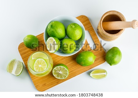 Lemonade with lemon, mortar and pestle in a glass on white and cutting board background, flat lay. 