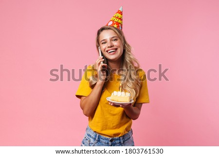 Image of happy positive birthday woman isolated over pink wall background holding cake with candle and talking by mobile phone