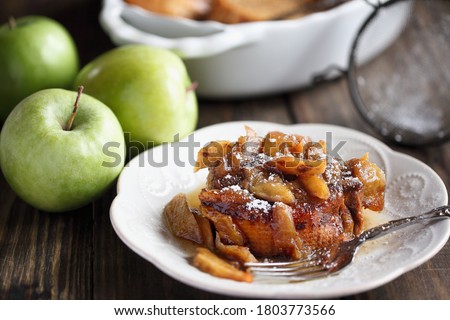 Serving of apple French toast casserole with maple syrup and powdered sugar. Selective focus with blurred background.
