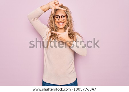Young beautiful blonde woman wearing casual sweater and glasses over pink background smiling making frame with hands and fingers with happy face. Creativity and photography concept.