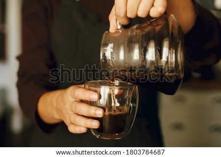 Professional barista in black uniform making drip coffee. Person pouring fresh aromatic coffee from glass kettle in cup. Alternative coffee brewing. Royalty-Free Stock Photo #1803784687