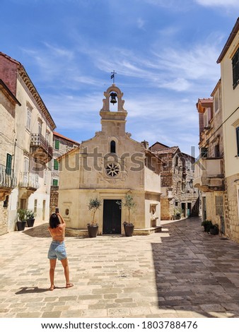 Female tourist taking photo of mall church on square of small urban village of Stari grad on Hvar island in Croatia, Adriatic Sea, Europe.
