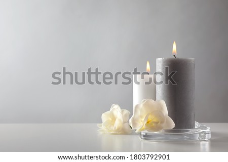 Wax candles and flowers in glass holder on table against light background. Space for text Royalty-Free Stock Photo #1803792901