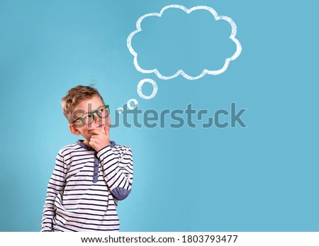 Schoolboy in glasses near blue wall with text cloud with space for your text. Thinking kid. Dream big. Back to school.