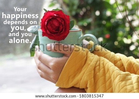 Inspirational motivational quote - Your happiness depends on you, and you alone. With young woman holding a cup of morning coffee or tea with red rose in hands. Create your own happiness concept.