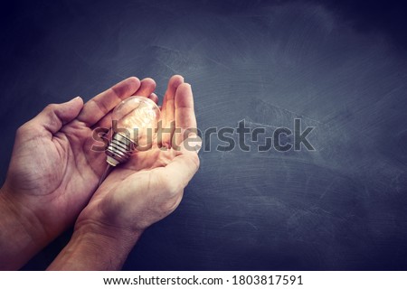 Education and business concept image. Creative idea and innovation. Man holding a light bulbs as metaphor over blackboard background