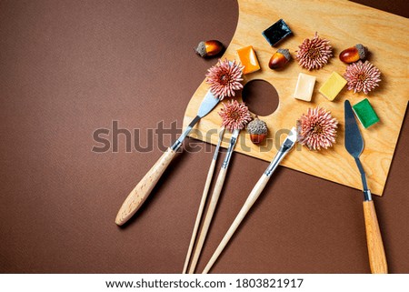Autumn still life with professional art materials, artist's palette, paints, brushes, acorns, autumn leaves on wooden background. Autumn concept. The workplace of the artist. Flat lay, top view