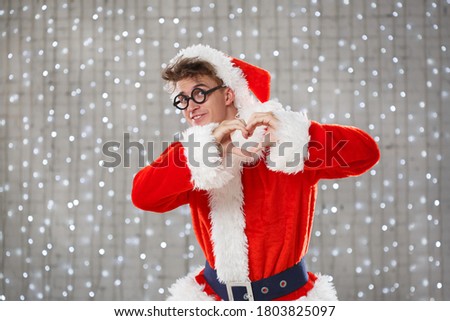 A young funny man in a santa claus costume folded his arms over his chest, making a heart with his fingers.