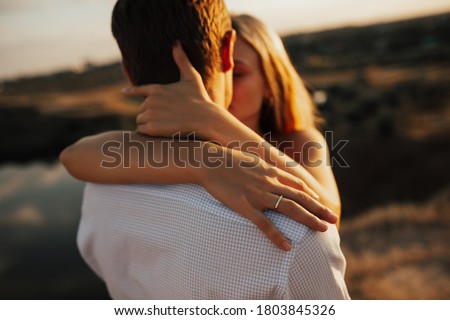 Focus on the woman's hand with engagement ring. Young wedding couple kissing in the field. Woman hugs man and kisses each other. Royalty-Free Stock Photo #1803845326