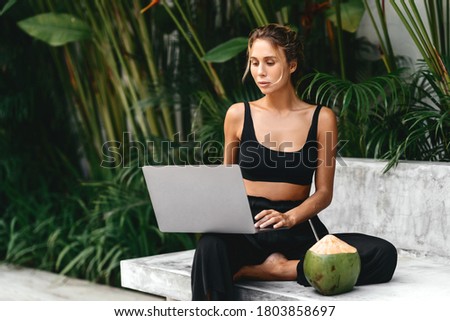 Woman working with laptop by the pool. Freelance work in tropical country