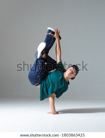 Cool b-boy dancing on one hand in studio isolated on gray background. Breakdance poster