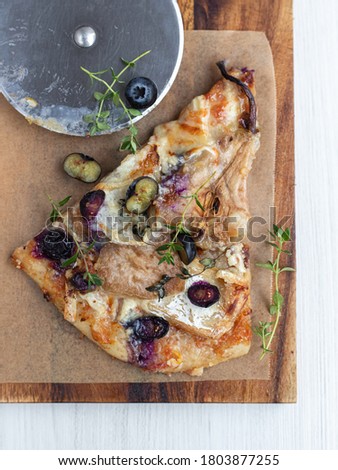 A piace of homemade rustic pizza with brie cheese, pears, blueberries and thyme