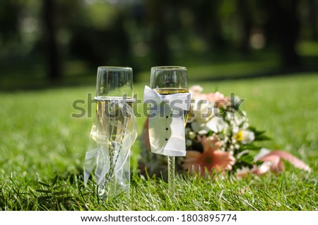 Two wedding glasses of champagne stand on the grass, against the background of a wedding bouquet. Sunny day. Close up