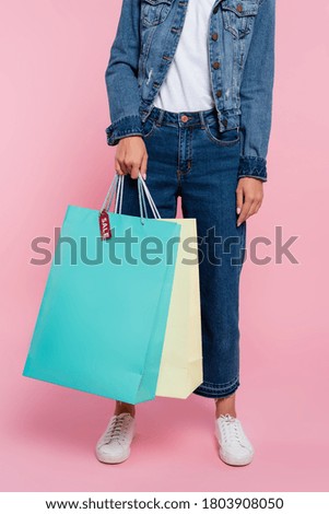 Cropped view of woman holding shopping bags with price tag and sale lettering on pink background