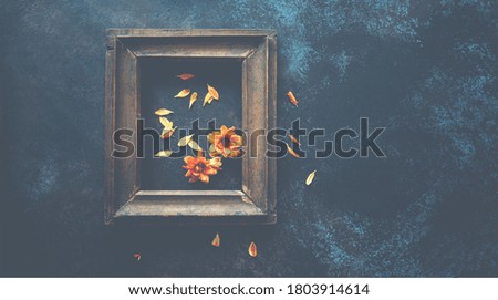 Old wooden frame with autumn flowers and leaves on brown rustic wooden background. Autumn flowers composition with copy space.