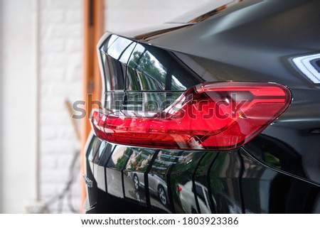 Side view of shiny black sedan with reflection on rear panel & body paint after car wash & ceramic coat. Concept of car detail and paint protection. Hi gloss finish background. Car paint & paint job. Royalty-Free Stock Photo #1803923386