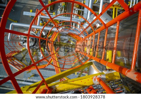 Looking down an industrial steel ladder with safety cage. Heavy industry gas and petroleum plant. Pov with sleective focus and vivid yellow, orange and reflective steel colors as safety first concept. Royalty-Free Stock Photo #1803928378