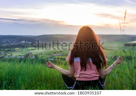 Photo of Young woman sitting back, meditate in lotus yoga pose outdoor, on the hill on the evening summer sunset