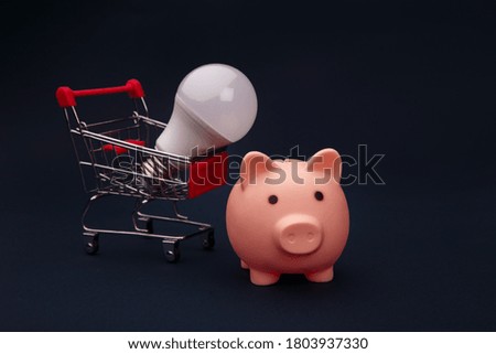 Piggy bank with trolley and lamp on dark blue background. Power saving concept