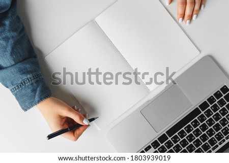 Female hand writing in a notebook on table with laptop, view from above