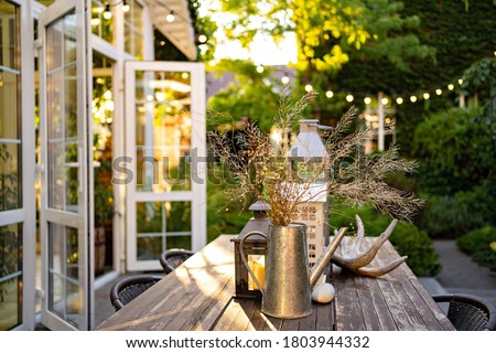 table for lunch outside in the garden in the courtyard with the lights of a country house at sunset. landscape design in the cottage. Royalty-Free Stock Photo #1803944332