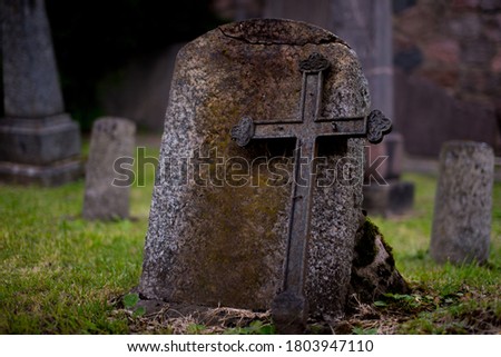 Blank tombstone. Empty old tombstone with old rusted cross on green background in old cemetery. Old metal cross with a stone. Copy space. Blank headstone in cemetery. Funeral, tombstone no inscription