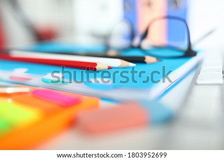 Close-up of bright colourful pencils on table. Blue notebook for creative ideas and thoughts. Black glasses. Working desktop with stuff. Mess on clerk desk. Business concept